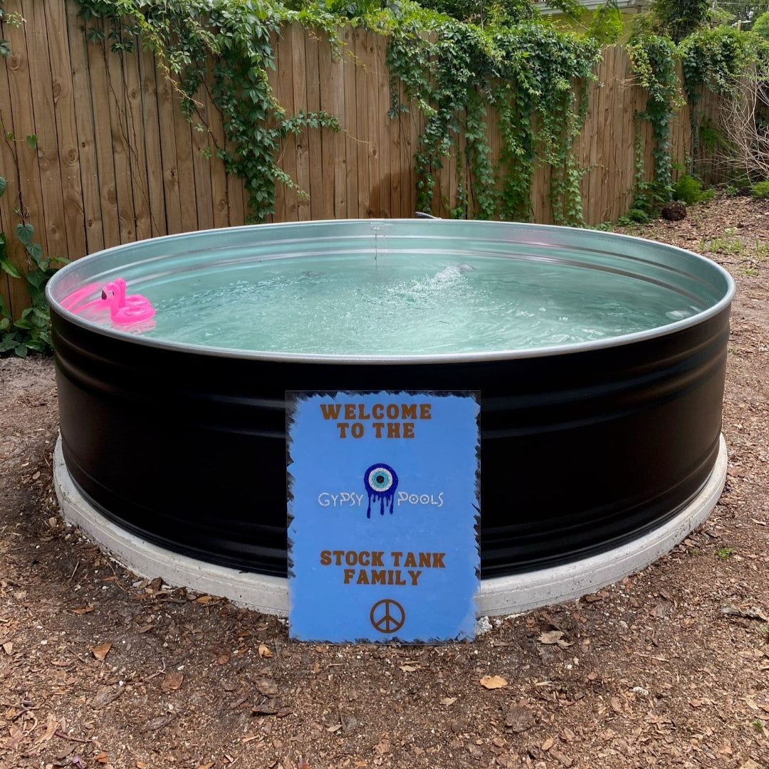 Stock tank pool with a pink float and a sign in a backyard setting.