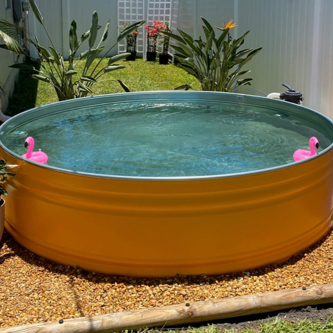 Yellow above-ground pool with pink flamingo floaties in a garden setting.