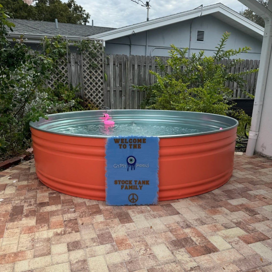Orange metal stock tank pool with a blue sign on a brick patio