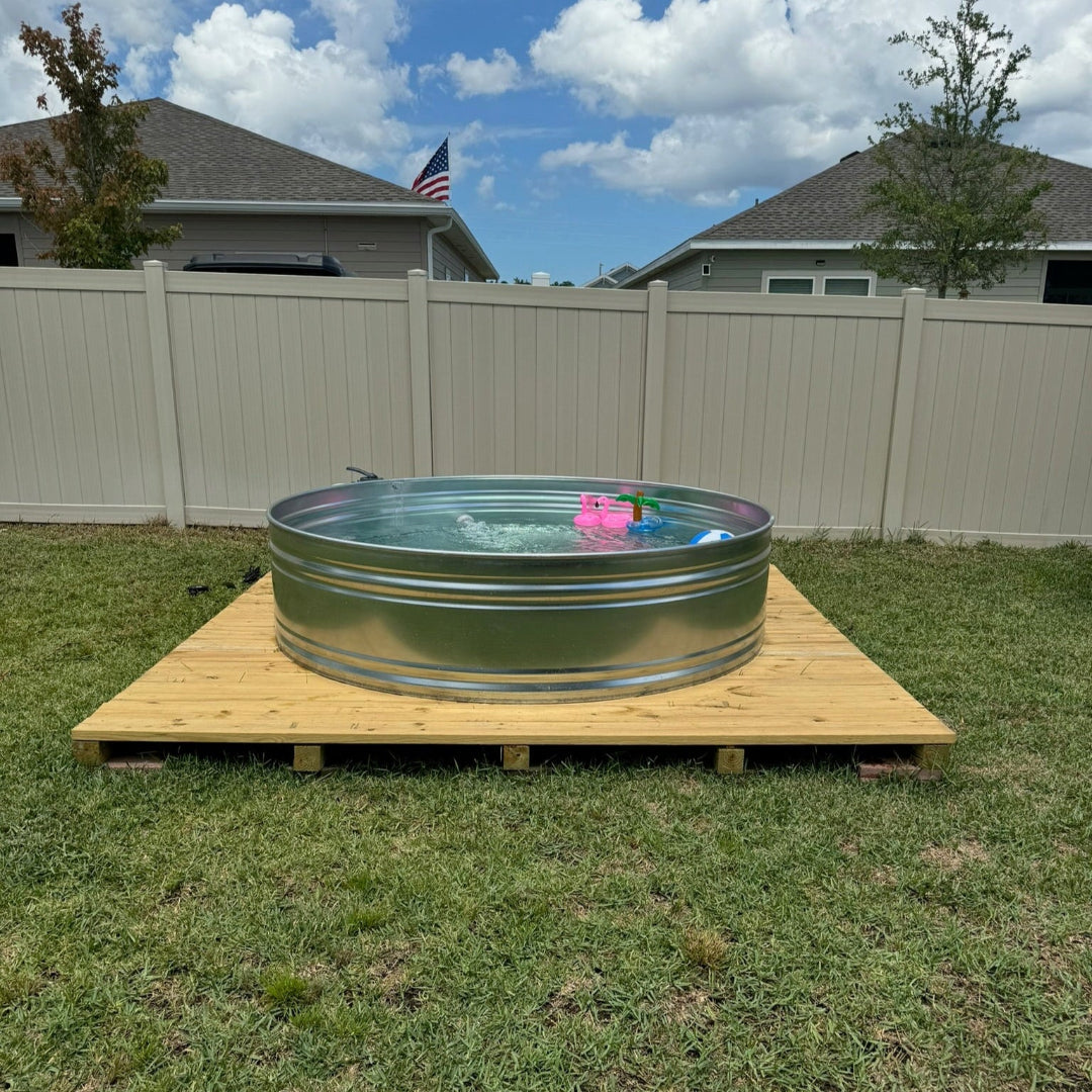 Metal tank pool on a wooden platform in a backyard with a grassy area and houses in the background.