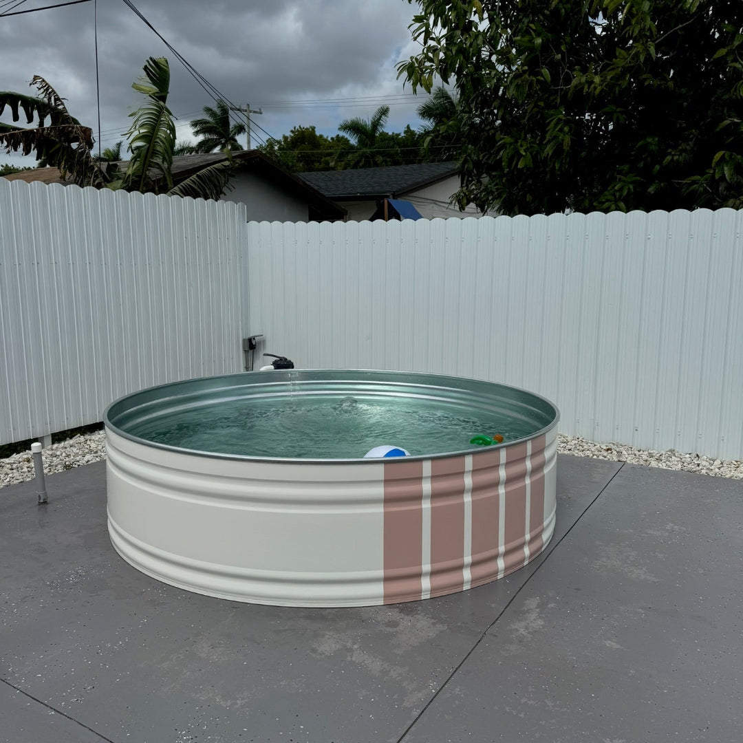 Small round pool with plaid design on a concrete surface, surrounded by a white fence and trees.