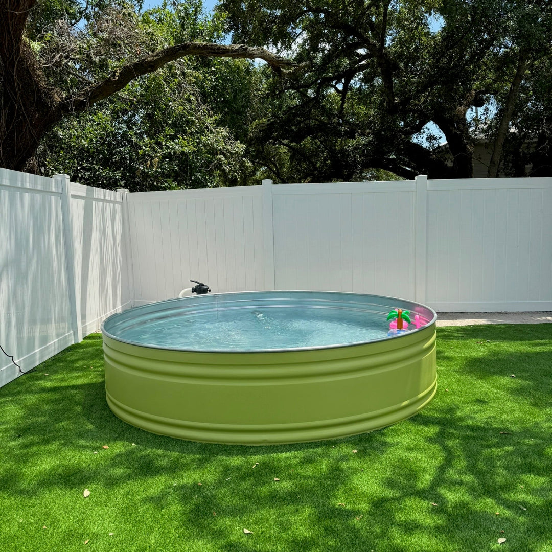 Green above-ground pool on grass with trees and white fence in the background