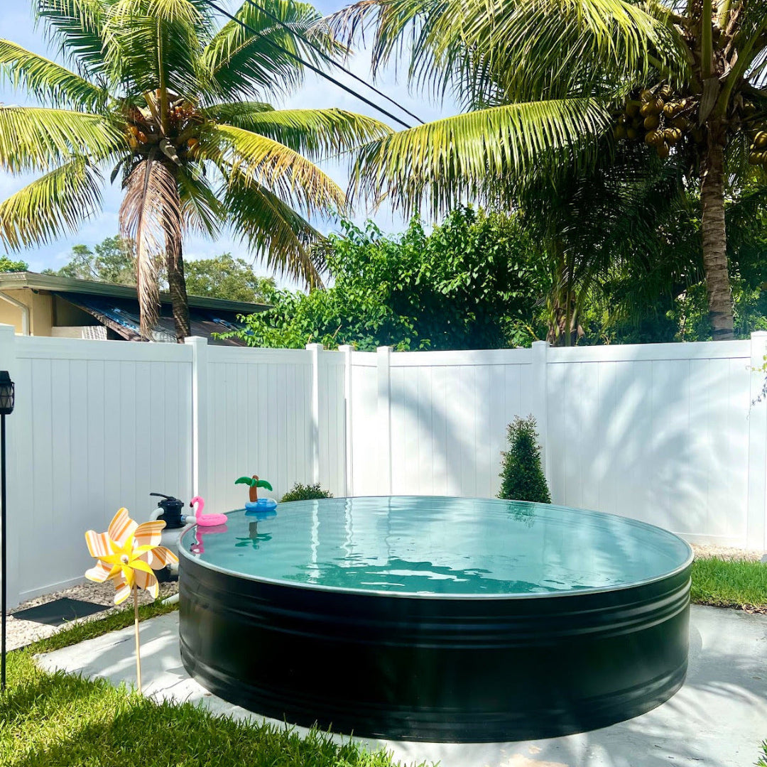 Portable pool in a backyard with palm trees and a white fence.