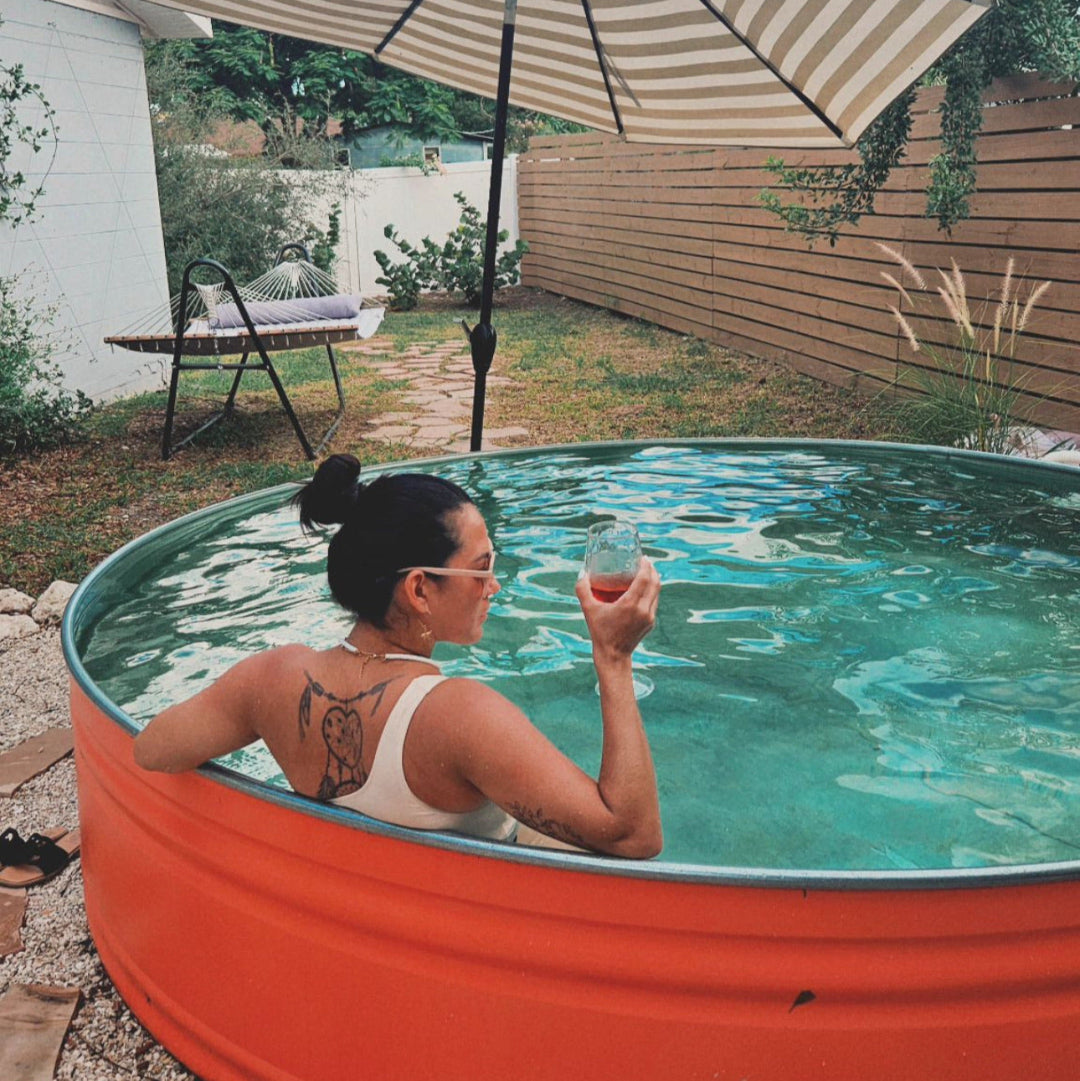 Person sitting in a small pool with a striped umbrella and garden chair in the background