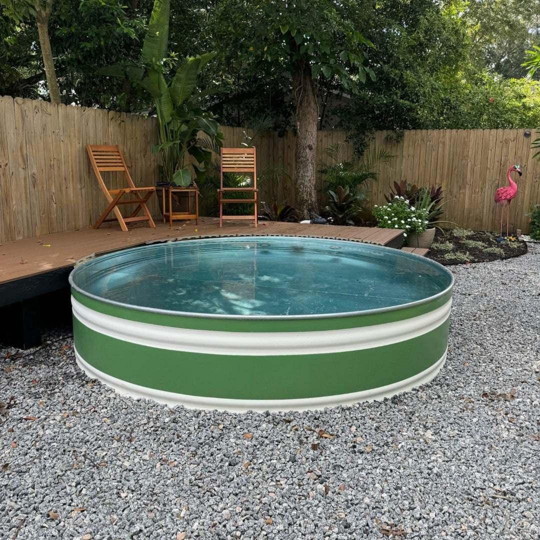 Green and white stock tank pool in a backyard setting with trees and wooden furniture.