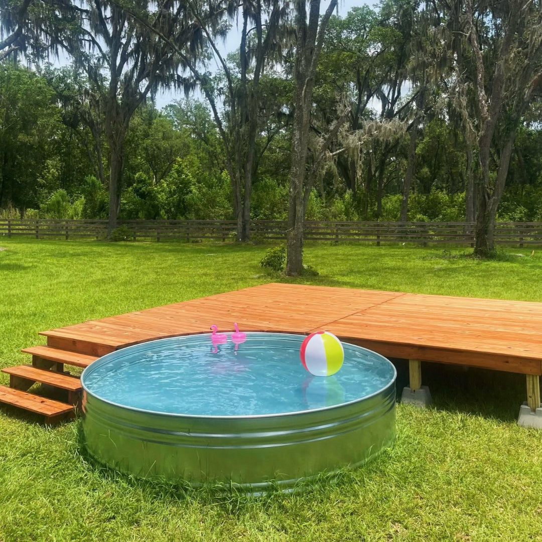 Metallic above-ground pool with toys on a grassy lawn next to a wooden deck.