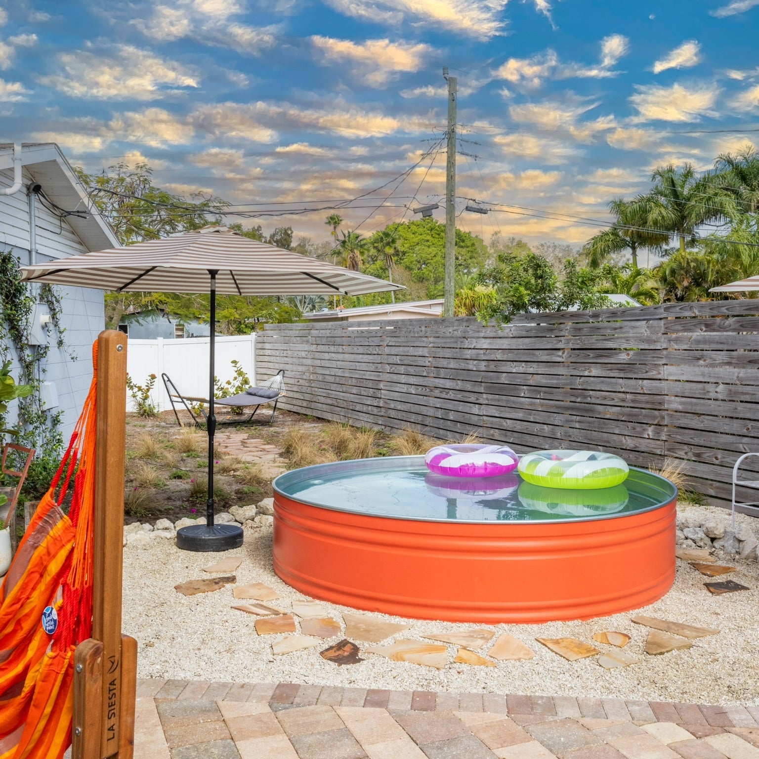 Outdoor setting with a small orange pool, inflatable toys, and a patio umbrella on a sunny day.