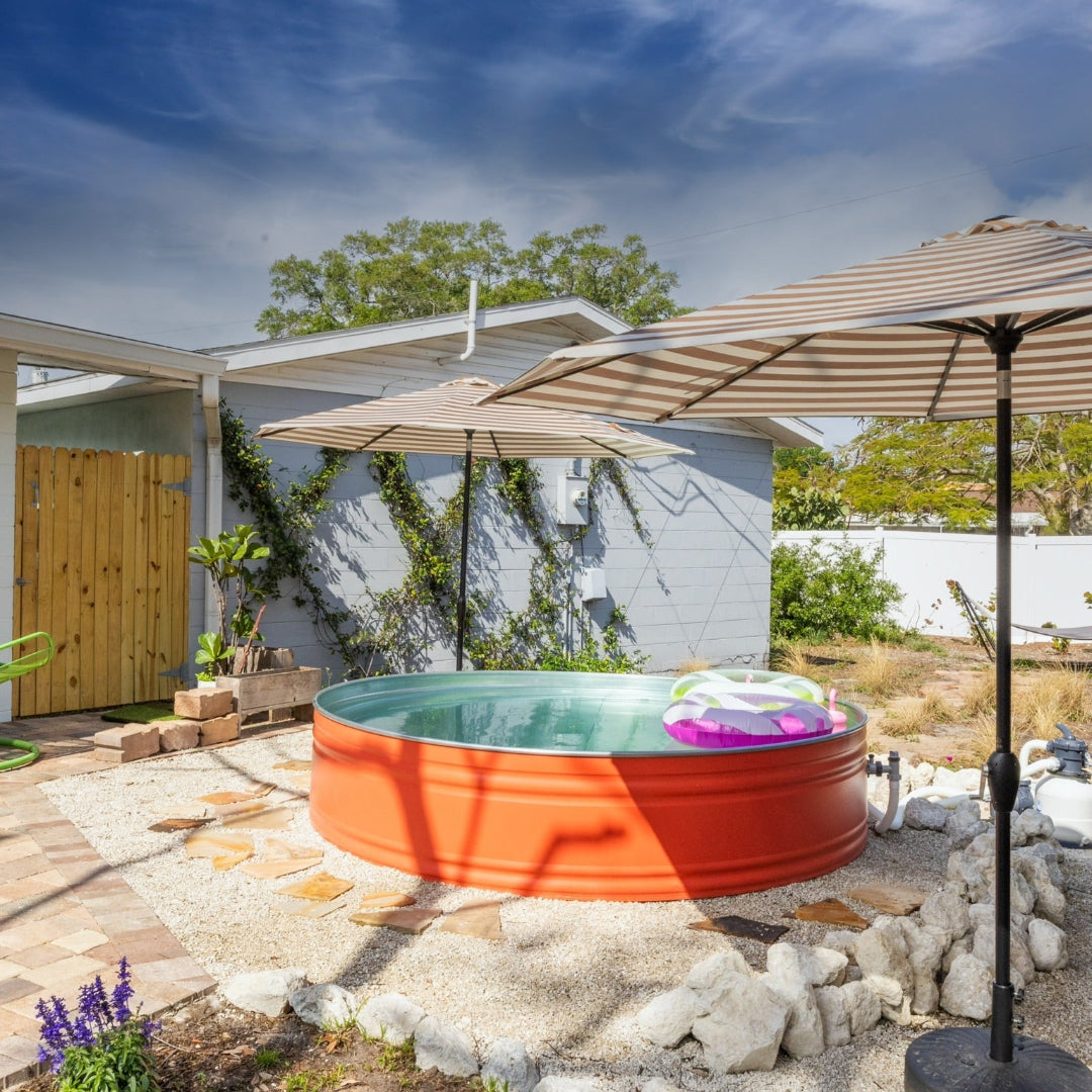 Small outdoor hot tub with orange exterior and white interior, surrounded by rocks and plants under a clear blue sky.