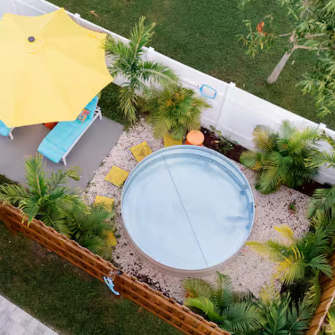 Circular pool surrounded by greenery and a yellow umbrella in a backyard setting.