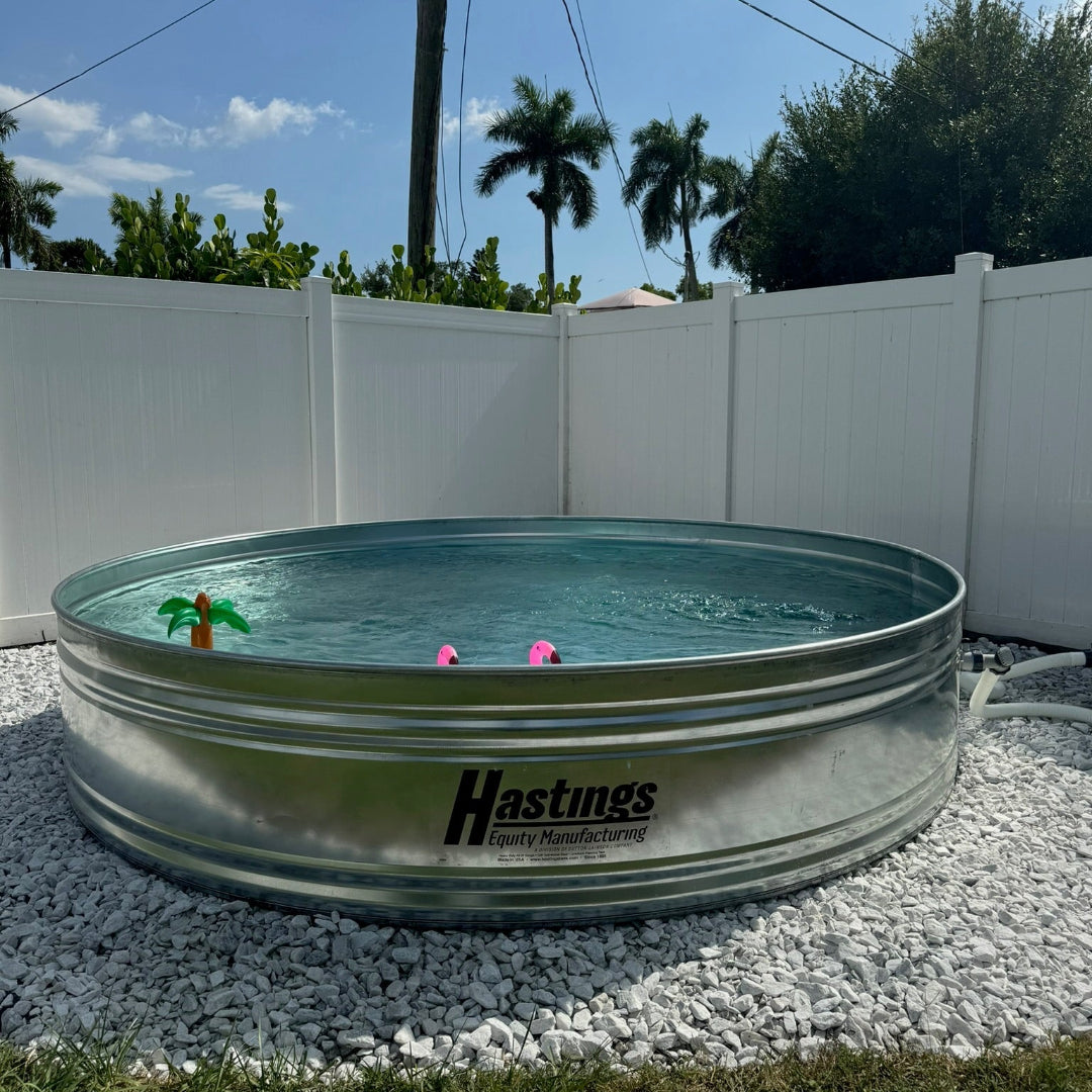 Metal water tank with 'Hastings' branding on a gravel surface with palm trees in the background.