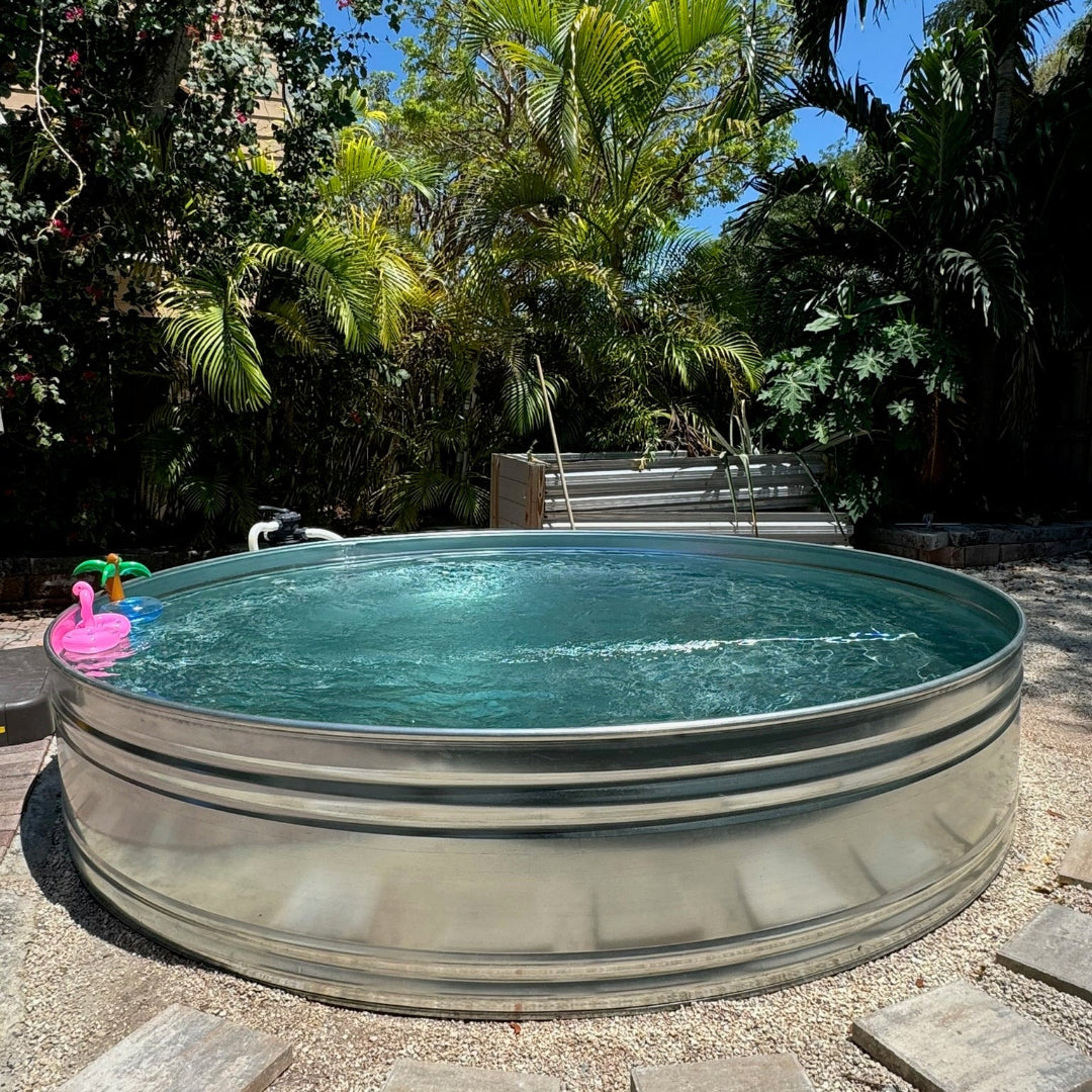 Metallic above-ground pool in a garden setting with trees and a clear blue sky.