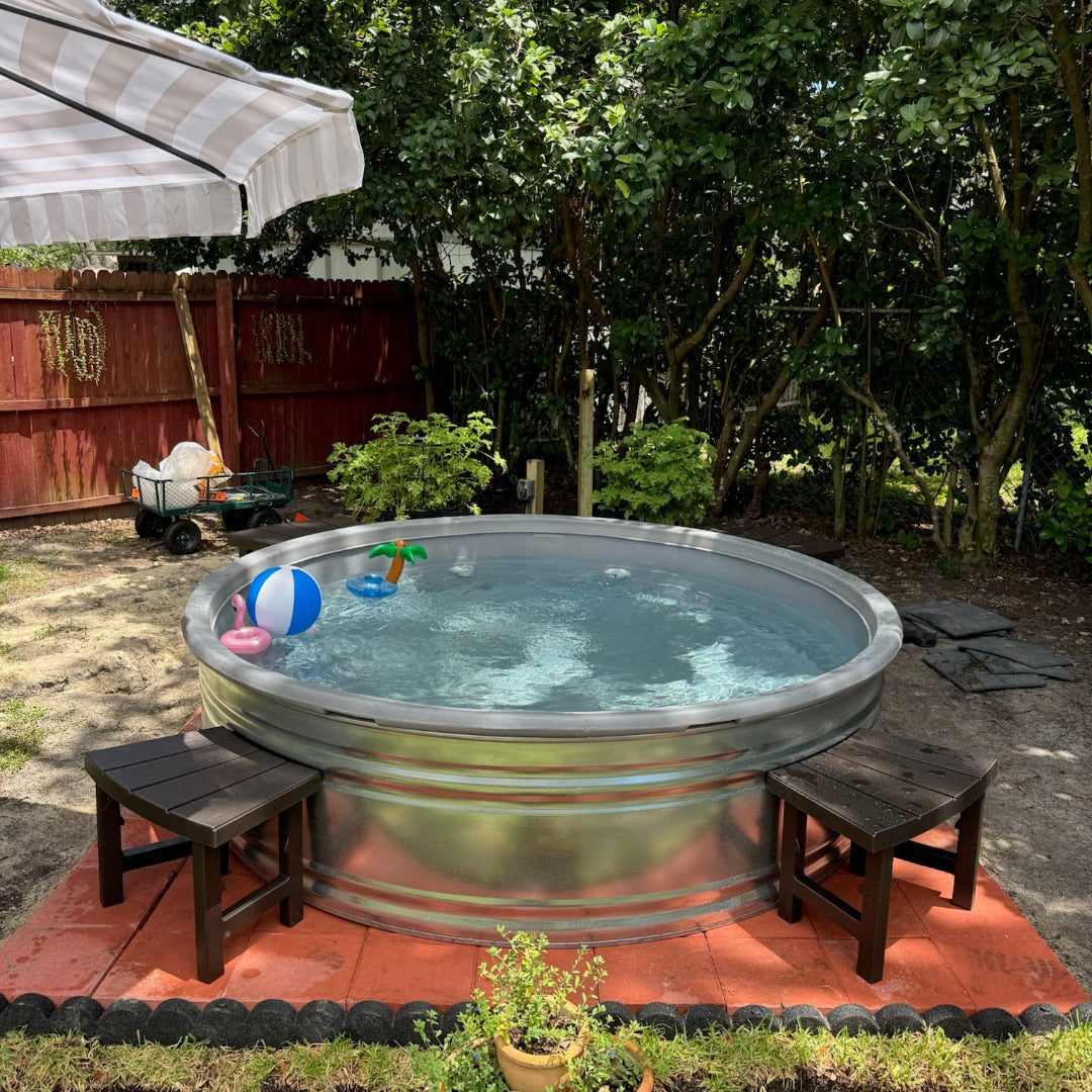 Metallic hot tub in a backyard setting with trees and a red fence.