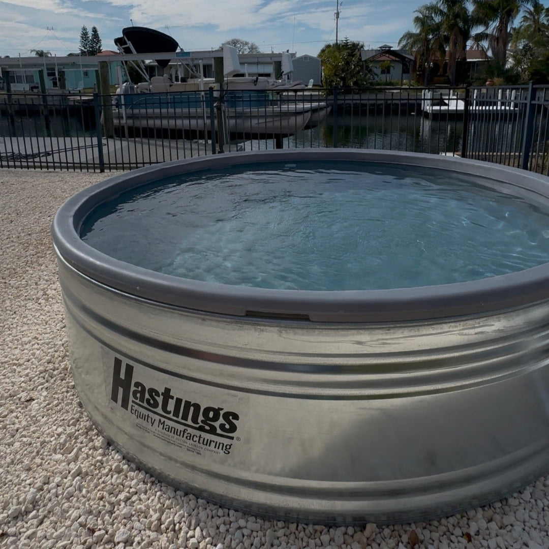Metal water tank with 'Hastings' branding on a gravel surface with a marina in the background.