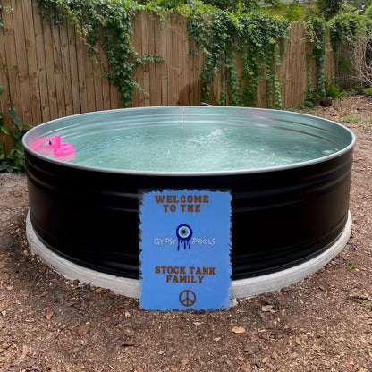 Stock tank pool with a pink float and a sign in a backyard setting.