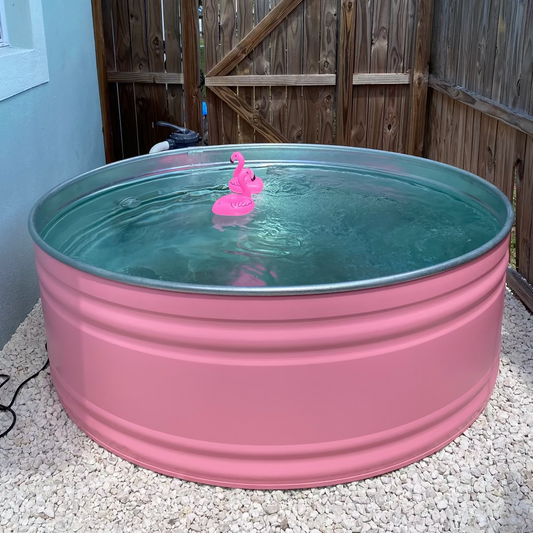 Pink metal tank with water and a pink flamingo toy in a backyard setting.
