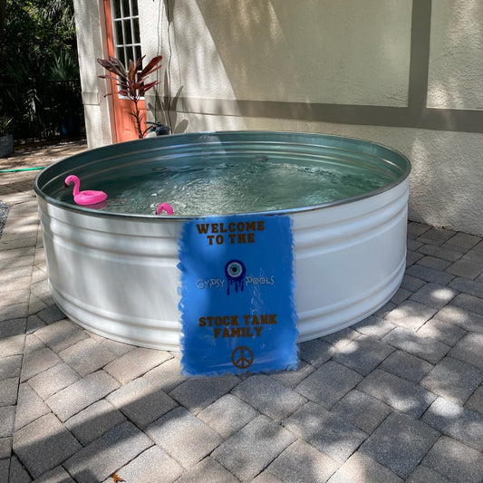 Metal stock tank pool with pink flamingo floaties and a blue sign in front of a house.