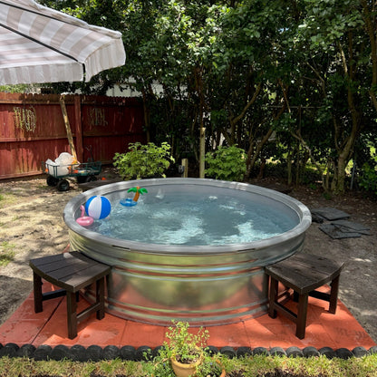 Metallic hot tub in a backyard setting with trees and a red fence.
