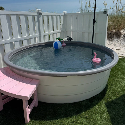 Small above-ground pool with toys on a grassy area next to a white fence.