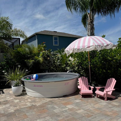 Portable hot tub on a patio with pink chairs and an umbrella in a backyard setting.